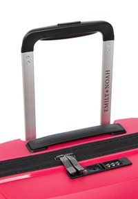 Tvrdý růžový kufr s texturovaným povrchem, černým zipem, teleskopickou hliníkovou rukojetí a integrovaným kombinačním zámkem.