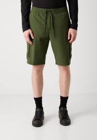 Grønne cargo-shorts med elastisk talje, sidelommer og en glat tekstur. Kombinert med sorte sneakers og ankelstore sokker.
