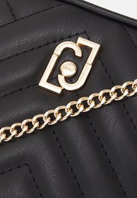 Czarna pikowana skórzana torebka na ramię z złotym łańcuchem i złotym logo. Powierzchnia ma teksturowane wykończenie.