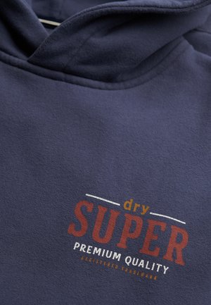 Granatowa bluza z kapturem z napisem "dry SUPER premium quality zarejestrowany znak towarowy" nadrukowanym na pomarańczowo, czerwono i biało na klatce piersiowej.
