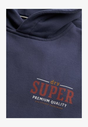 Granatowa bluza z kapturem z napisem "dry SUPER premium quality zarejestrowany znak towarowy" nadrukowanym na pomarańczowo, czerwono i biało na klatce piersiowej.