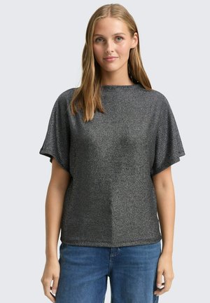 Korte mouw top gemaakt van zwarte textuurstof met zilveren spikkels. Heeft een losse pasvorm en een ronde halslijn. Gecombineerd met blauwe denim jeans.