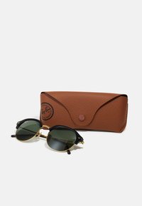 Ochelari de soare Ray-Ban cu lentile rotunde întunecate; rame negre cu accente aurii. Include un toc din piele maro texturată.