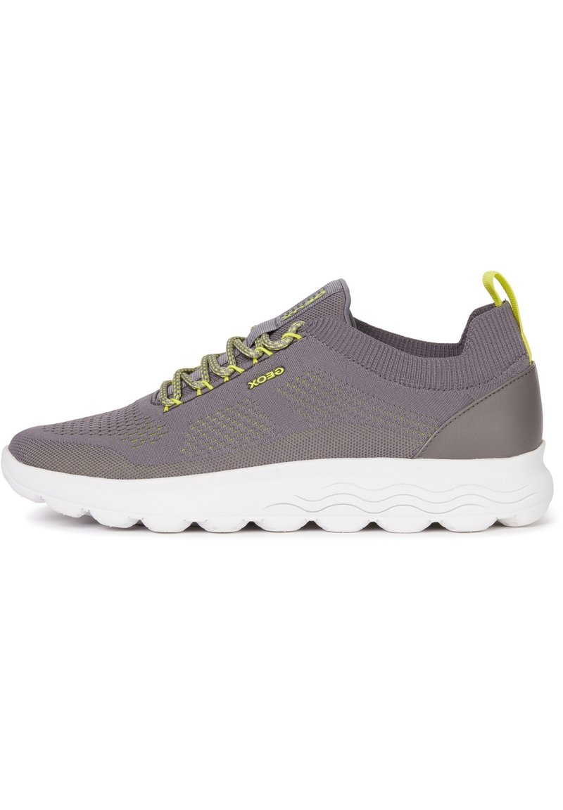 Zapatilla textil gris con suela blanca flexible, que presenta cordones verdes y un cuello acolchado para mayor comodidad y soporte.