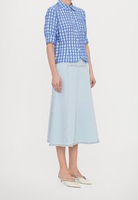 Camicia a maniche corte a quadri blu e bianchi, abbinata a una gonna midi in denim blu chiaro e mule beige senza lacci.