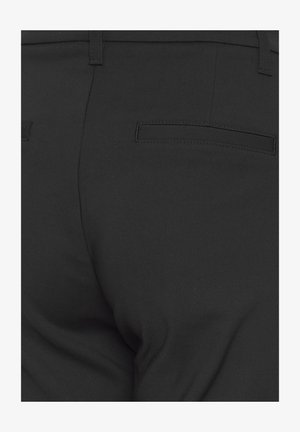 Zwarte, op maat gemaakte broek met twee achterste insteekzakken en riemlussen, gezien vanaf de taille naar beneden.