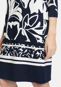 Blumenmuster-Kleid in Marineblau und Weiß. Hergestellt aus weichem Stoff, mit Dreiviertelärmeln und einer taillierten Silhouette.