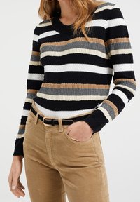 Stickad tröja med horisontella ränder i svart, vitt, beige och brunt. Ribbad textur och rund halsringning. Kombinerad med bruna kordflortbyxor.