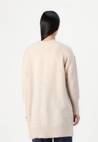 Béžový oversized svetr s jemným texturovaným povrchem, s padlými rameny a žebrovaným lemem. Dlouhé rukávy a kulatý výstřih.