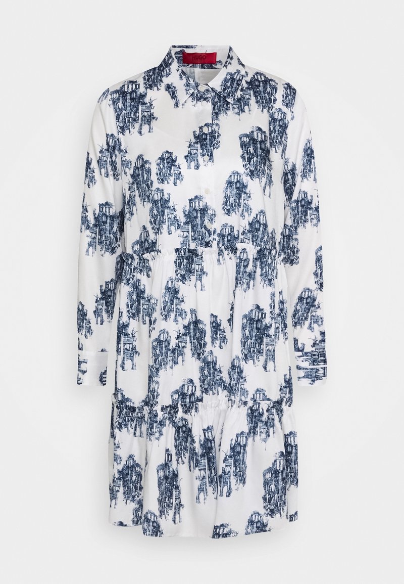 Robe blanche avec imprimé bleu présentant des motifs architecturaux, fermeture à boutons sur le devant, col, taille froncée, manches longues et ourlet à volants.