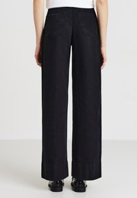 Pantaloni in denim neri a vita alta con design a gamba larga, tasche posteriori e orlo grezzo. Tessuto strutturato con un aspetto liscio.