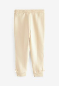 Pantalons tapered beiges clairs en tissu doux, dotés d'une taille élastique et de petits nœuds au bas. Texture lisse et design minimaliste.