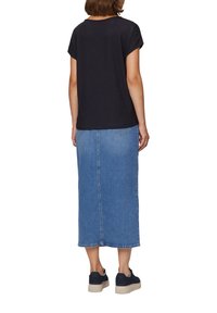 Czarny top o teksturowanej powierzchni z krótkimi rękawami, w połączeniu z niebieską, długą spódnicą dżinsową. Model nosi ciemne tenisówki, na spódnicy widoczne przeszycia i kieszenie.