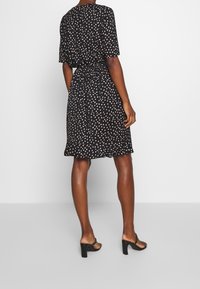 Robe noire à manches courtes, ornée d'un motif à pois blancs, avec une taille élastique et un ourlet évasé. Portée avec des sandales à talons blocs.