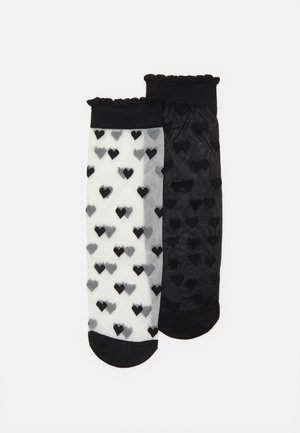 Černo-bílé vzorované ponožky ke kolenům s designem srdíček, vyrobené z průhledného materiálu, s volánkovými lemy a kontrastními prsty a patami.