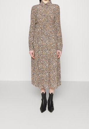 Femme porte une robe midi à manches longues avec un petit motif floral en marron, blanc et noir, associée à des bottines noires à bout pointu.