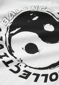 Camiseta blanca con un gran diseño negro de yin-yang con salpicaduras, y la palabra "BALANCE" alrededor de la parte superior en letras negras y en negrita.