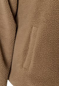 Καφέ υφασμάτινο fleece με υφή και κατακόρυφο ορθογώνιο άνοιγμα τσέπης ραμμένο στο υλικό.