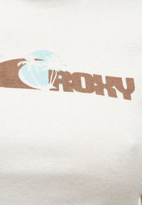 Καφέ κείμενο "ROXY" με γραφικό δύο ανοιχτόμπλε φοίνικων σε λευκό ύφασμα.