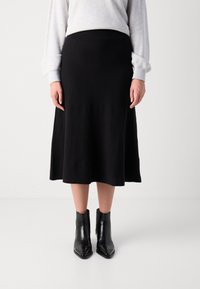 Zwarte knie-lange rok van gebreide stof met een gladde textuur. Draagt een strakke zwarte enkellaarsjes en een lichtgrijze sweatshirt.