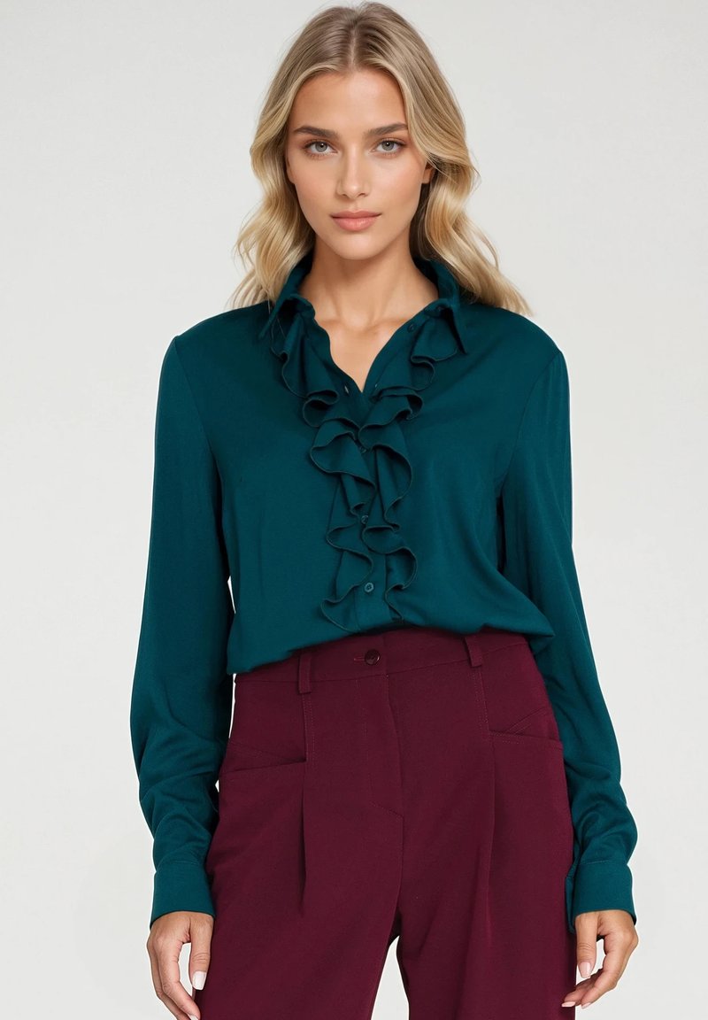 Turkusowa bluzka z falbanami z przodu, długimi rękawami i spiczastym kołnierzykiem. W zestawieniu z bordowymi spodniami o wysokim stanie. Gładka tekstura materiału.