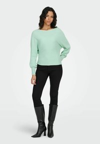 Hele mintroheline kudumiga kampsun, lahtine lõige, soonikuline tekstuur ja pikad varrukad. Sobitatud mustade kitsaste teksade ja põlvekõrguste kontsadega saapadega.