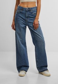 Light blue, high-waisted wide-leg jeans with a straight cut. Made of denim, featuring front pockets and a zipper closure. Distressed hem detailing.