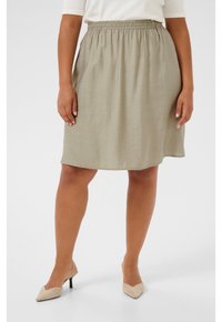 Jupe kaki verte de longueur genou en tissu léger et texturé avec une taille élastique. Associée à des escarpins beiges à bout pointu.