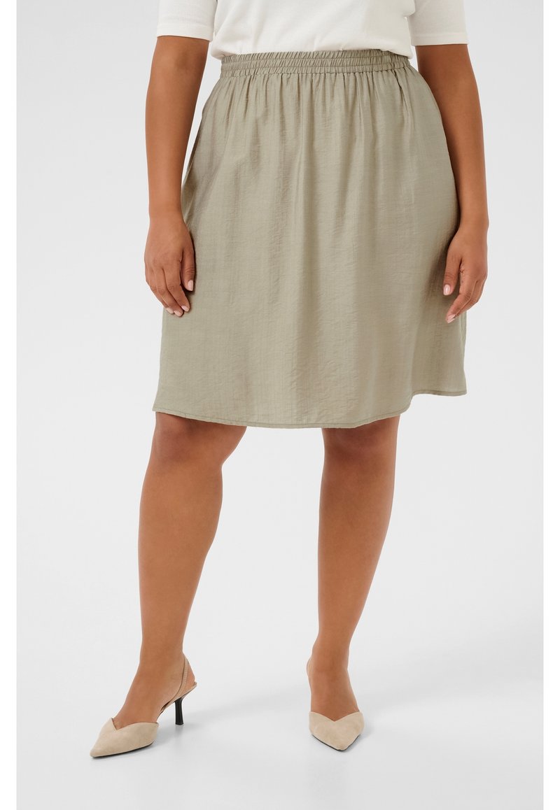 Jupe kaki verte de longueur genou en tissu léger et texturé avec une taille élastique. Associée à des escarpins beiges à bout pointu.