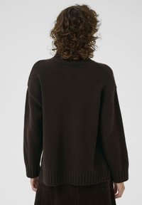 Pull en maille marron foncé avec un col montant, des épaules tombantes et des poignets côtelés. Texture douce avec une coupe décontractée.