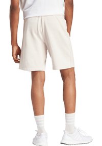 Pantaloni corti in cotone beige con elastico in vita, caratterizzati da una texture liscia, taglio dritto e dettagli sulle cuciture laterali. Indossati con calzature bianche.