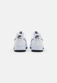 Fehér bőr Nike Air sportcipők fekete részletezéssel, alacsony felső résszel, texturált sarokkal és gumitalppal. Jellemzője a logó a sarokon és a nyelvén.