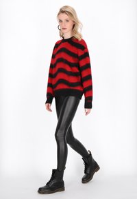 Maglione a righe rosse e nere con una vestibilità rilassata, abbinato a leggings neri lucidi e stivali neri con lacci. Texture morbida e colori audaci.
