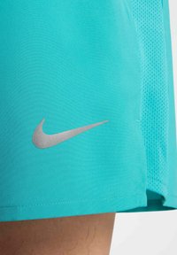 Turkoosi urheilushortsit, joissa on sileä kangas, ja joissa on hopea Nike-logo sekä verkkopaneelityksellä sivuilla.