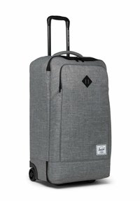 Valise à roulettes en tissu gris avec poignée télescopique, poche zippée à l'avant et écusson en forme de diamant noir sur le panneau avant.