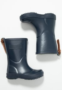 Botas de lluvia de goma azul marino con un acabado brillante, suelas texturizadas y detalles en cuero marrón que presentan un logo rectangular en la parte frontal.