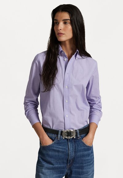 Hellblaues Langarmhemd mit Button-Down-Kragen, kombiniert mit blauen Jeans und einem schwarzen Gürtel mit dekorativer silberner Schnalle.