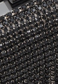 Gros plan sur des pierres noires facettées montées sur des griffes en argent, formant un motif en grille dense et scintillant sur une surface texturée.