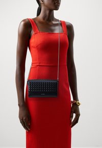 Borsa a tracolla in pelle intrecciata nera con base liscia, tracolla in catena argentata, forma rettangolare e un delicato dettaglio del logo sul davanti.