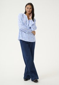 Blouse florale bleu clair avec des manches bouffantes, assortie à un pantalon en denim foncé à jambes larges. Tissu lisse, coupe décontractée et détails de motif subtils.