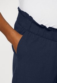 Námořnicky modré kalhoty s elastickým pasem se stahováním a bočními kapsami, vyrobené z lehké látky s hladkou texturou.