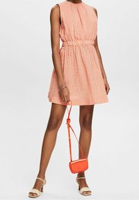 Robe sans manches à rayures rouges et blanches avec une taille élastique, associée à des sandales à talons blocs beiges et un petit sac crossbody orange.
