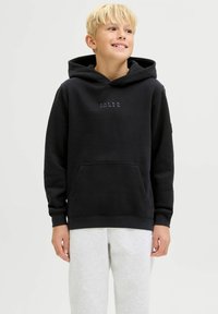 Felpa nera con cappuccio, tasca frontale, cordoncino e testo del logo in grigio. Il tessuto sembra morbido, indossato sopra pantaloni della tuta grigio chiaro.