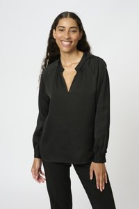Blusa nera a maniche lunghe con scollatura a V, caratterizzata da un tessuto testurizzato e spalle arricciate. Indossata con pantaloni neri coordinati.