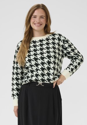 Zwart-wit geblokt gebreid sweater met een ronde halslijn en geribde manchetten, gedragen over een hoge taille zwarte broek met een riem.