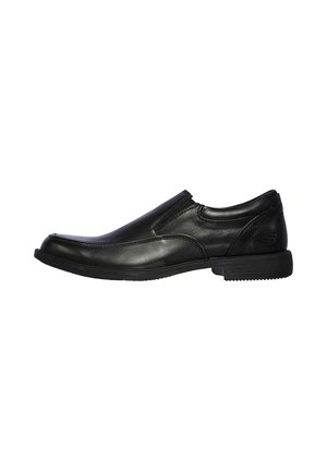Zapato negro de piel sin cordones con una superficie lisa, puntera redondeada, detalles de costura sutiles y una suela baja de goma. Diseño simple para un fácil uso.