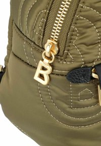 Sac en tissu gonflé vert olive avec zip doré et un charm logo "B" doré prominent, présentant des motifs de couture subtils et des accents en cuir noir.