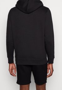 Svart hoodie med dragsko i huvan, tillverkad av mjukt tyg, med ribbade muddar. Kombinerad med matchande svarta shorts, båda är avslappnade kläder.