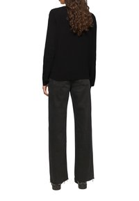 Pull noir à texture avec des manches longues, associé à un pantalon noir à taille haute et à jambes larges, avec des ourlets effilochés et des bottes cloutées.