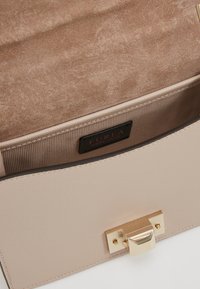 Borsa a mano in pelle beige con finitura texture, hardware dorato e chiusura magnetica. L'interno presenta una fodera liscia e un'etichetta di marca.